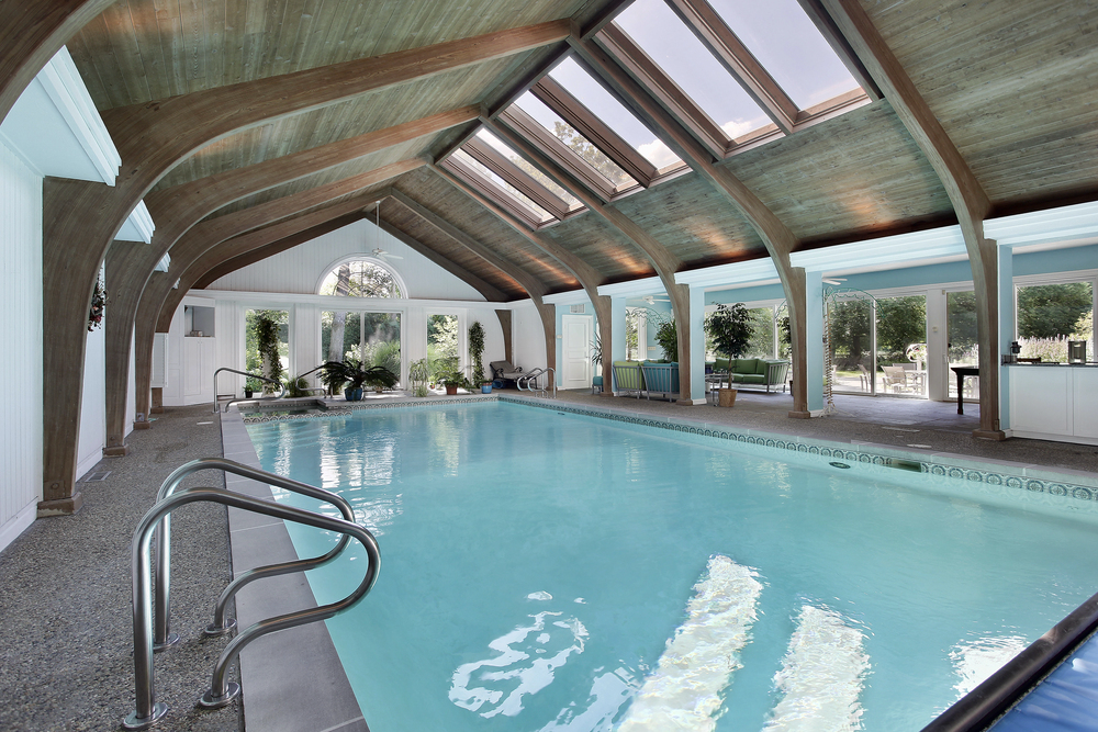 Custom pool enclosures featuring an indoor swimming pool beneath a vaulted wood ceiling and skylights